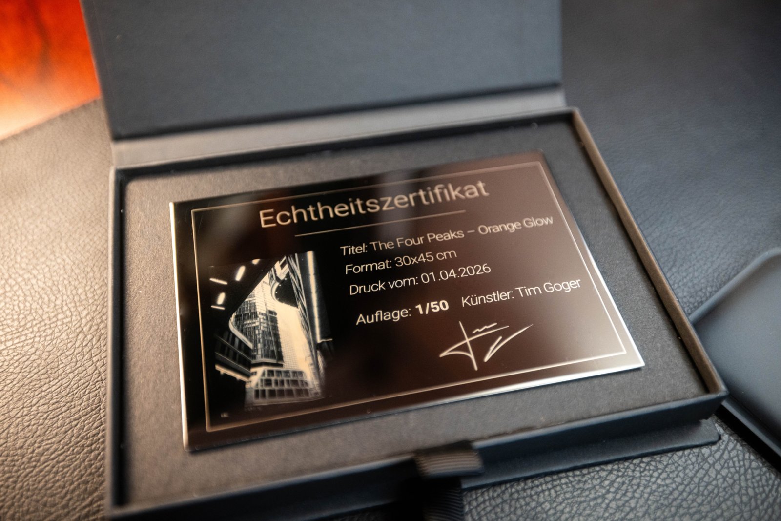 Graviertes Edelstahl-Echtheitszertifikat mit Signatur und Auflagennummer neben einem limitierten FineArt Kunstdruck fürs Büro.