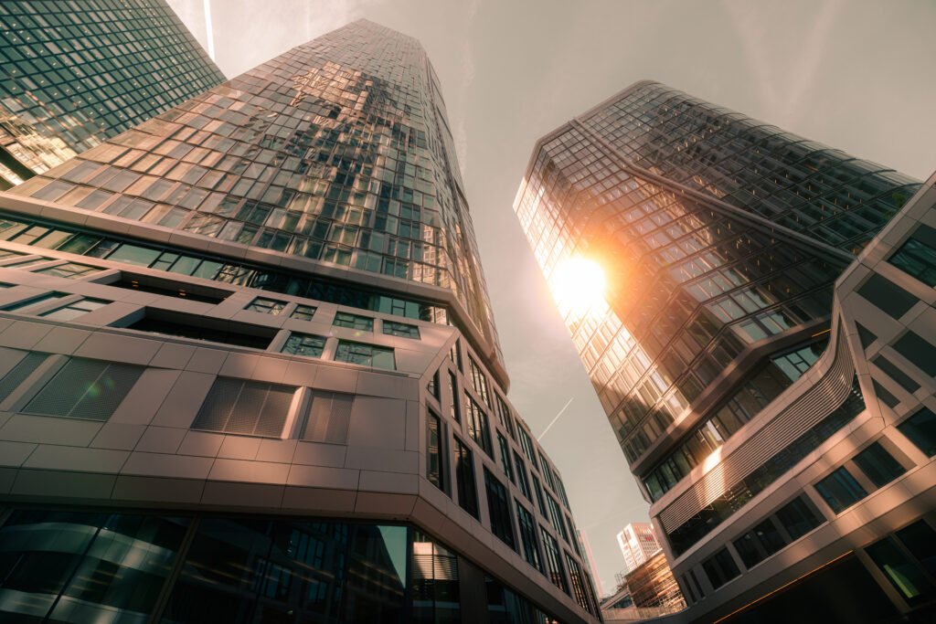 Froschperspektive auf zwei Glashochhäuser des 4-Tower Komplexes in Frankfurt mit Sonnenstrahlen und Lens Flare zwischen den Türmen.