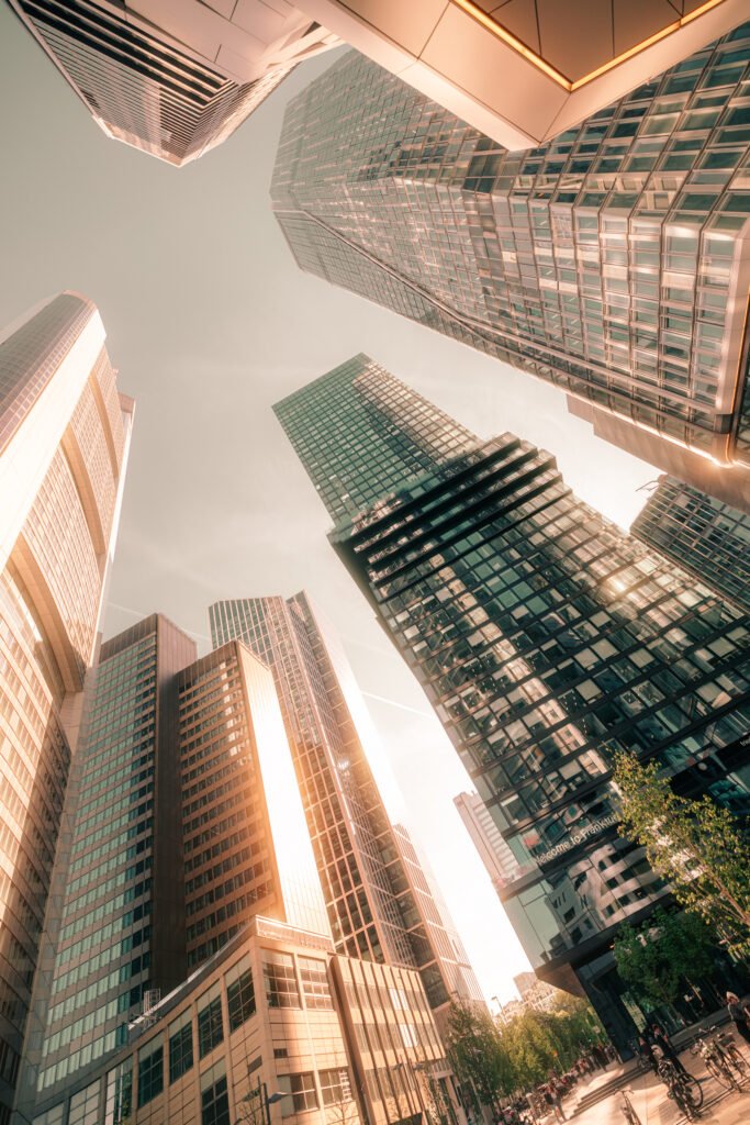 Froschperspektive auf die Frankfurter Skyline mit mehreren Hochhäusern aus Glas und Beton im warmen Gegenlicht der goldenen Stunde.