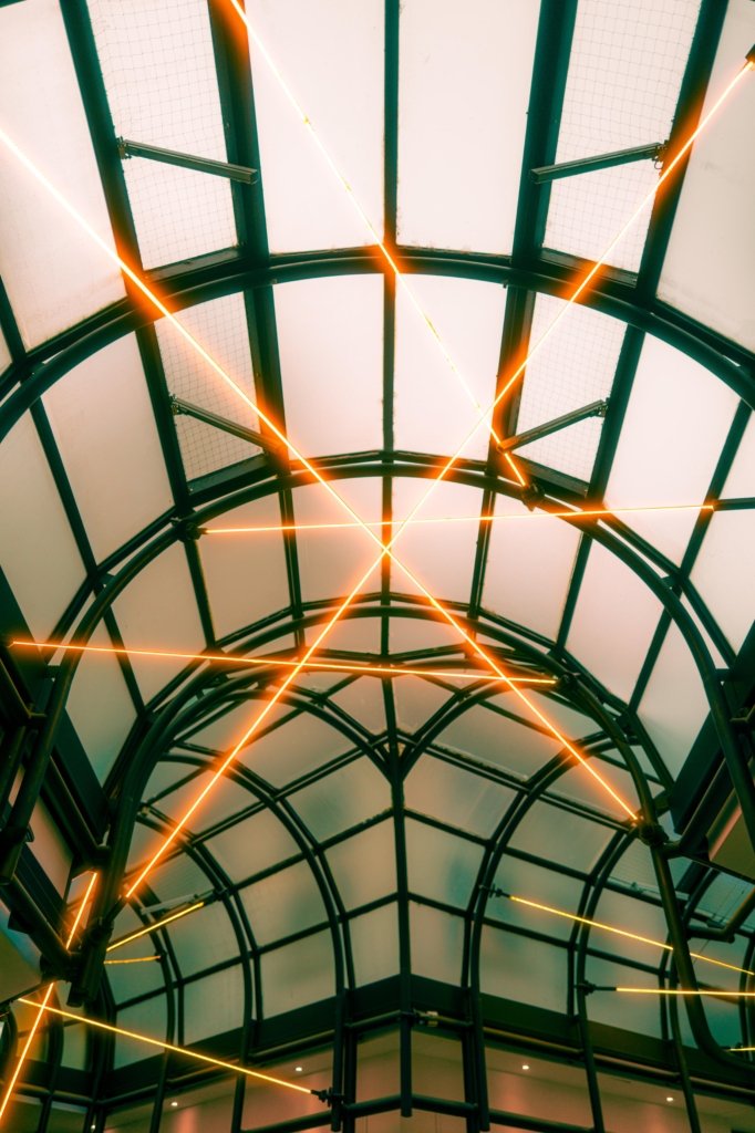 Blick nach oben in die gläserne Kuppelkonstruktion der Passage am Rossmarkt Frankfurt, dunkelgrüne Stahlbögen mit diagonal verlaufenden orangefarbenen Neonlichtstreifen als Kunstinstallation.
