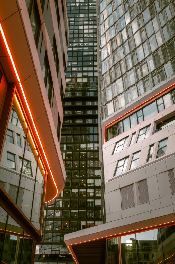 Blick von unten zwischen den modernen Glastürmen der 4-Tower Frankfurt, flankiert von leuchtenden orangen Neonstreifen an den Fassaden, Nachtaufnahme, urbane Architektur.